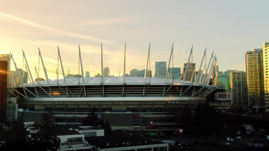 A slow cinematic aerial pullback shot of BC Place stadium surrounded by the Vancouver city skyline during a beautiful golden hour sunset