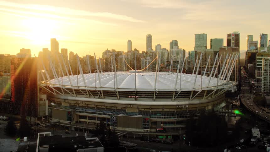 A dramatic aerial shot reveals the iconic BC Place stadium and the Vancouver skyline during a stunning golden sunset