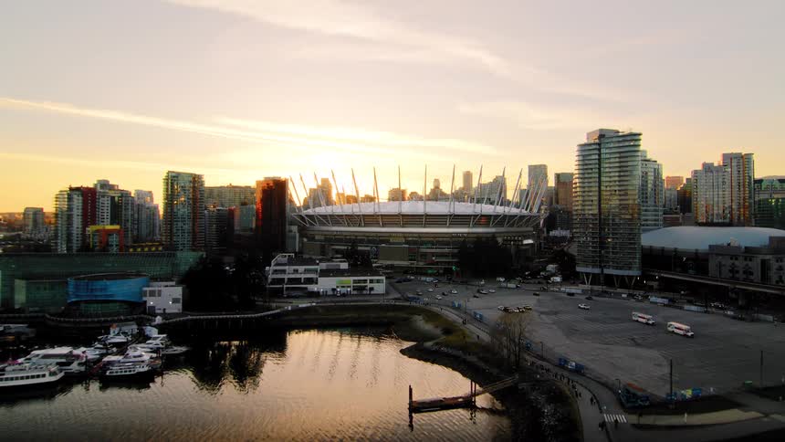 An epic aerial pull-back reveals the stunning BC Place stadium and the Vancouver city skyline glowing in the warm light of sunset over the water