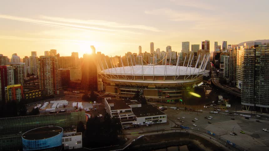 An epic aerial view captures the iconic BC Place stadium and Vancouver skyline, bathed in the warm golden light of a setting sun