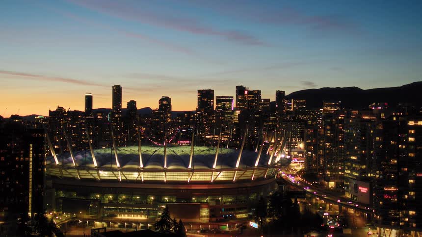Aerial pull-back of Vancouver's BC Place stadium and downtown skyline illuminated at sunset