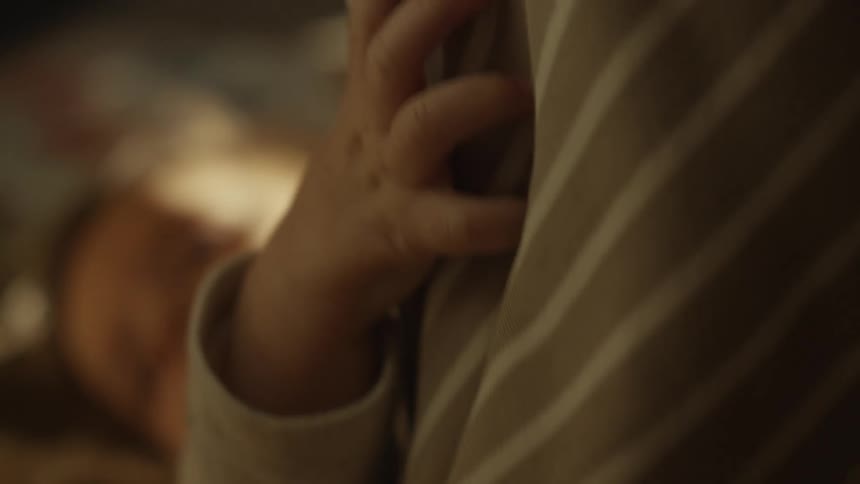 An intimate close-up of a toddler's hand gripping striped clothing in a warm, softly lit room