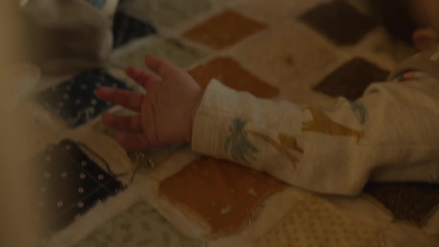 A soft focus close-up on a baby's tiny hand resting on a colorful patchwork quilt