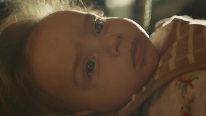 A serene baby with curious eyes lies still, bathed in warm, natural light