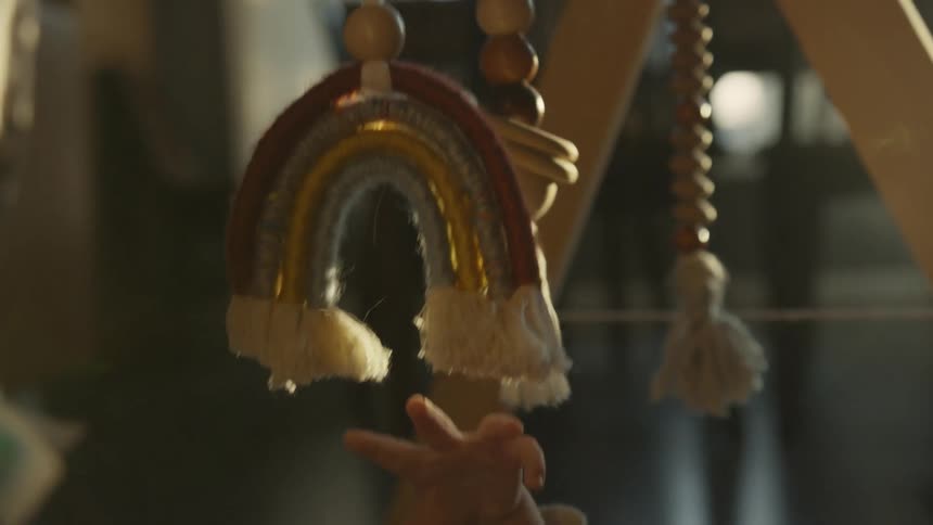 An infant's tiny hand reaches out to touch a colorful rainbow mobile hanging from a wooden play gym