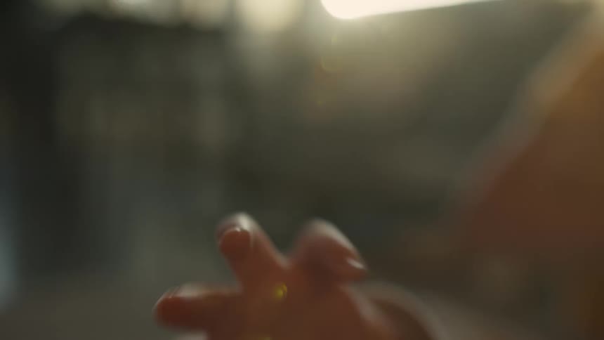Soft-focus close-up of a baby's hand twitching and reaching with warm, gentle light and lens flare