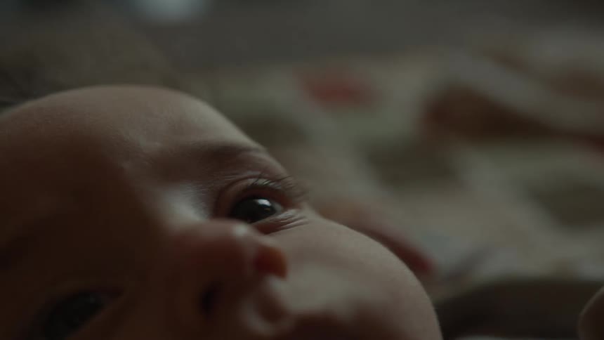 An intimate extreme close-up of a newborn baby's face and curious eyes as they lay peacefully in soft, low light