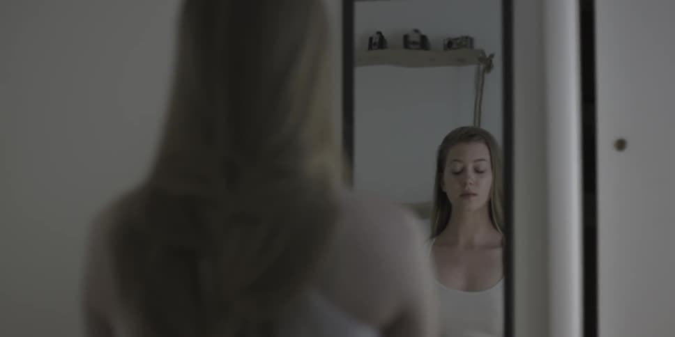 A long haired girl stands in front of a mirror