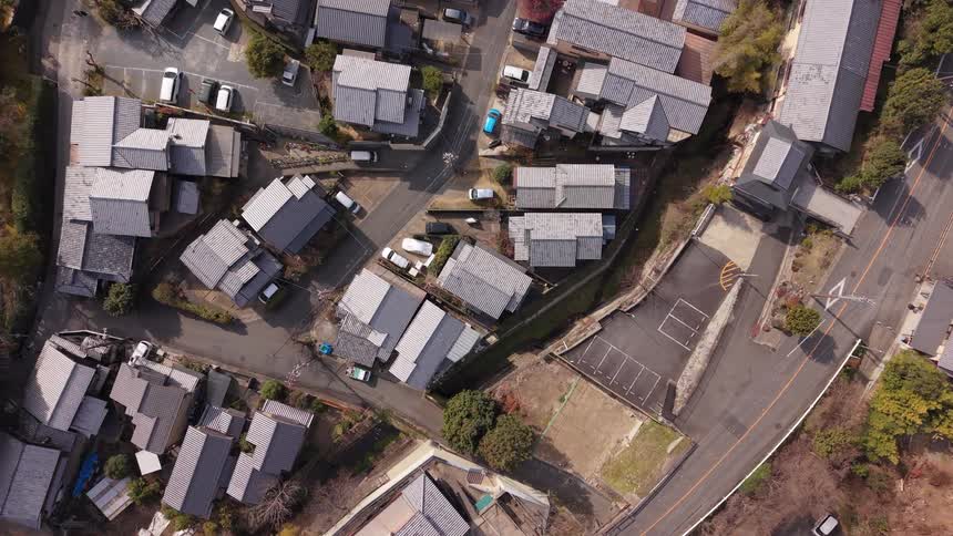 A slowly rotating top-down aerial view of a quiet, traditional Japanese village with distinctive gray tiled roofs