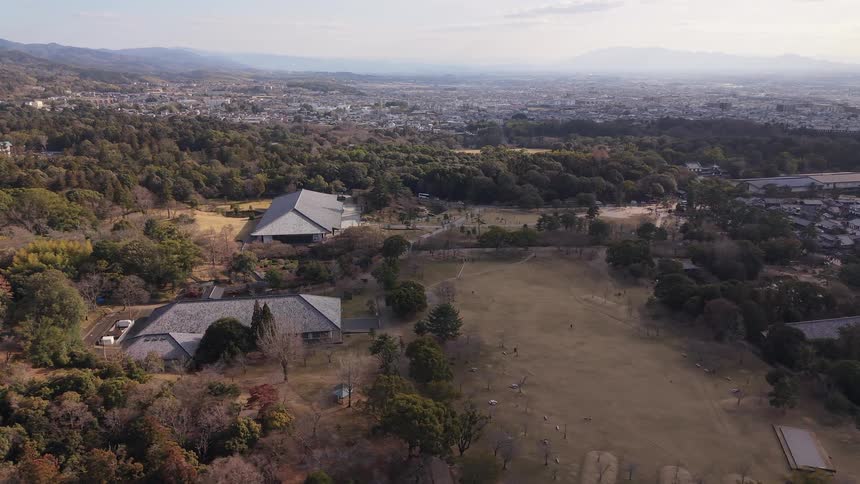 A static aerial timelapse overlooks Nara Park in Japan, with the Nara National Museum and the sprawling city visible under a hazy sky
