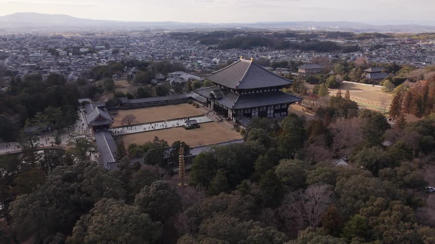 Slow aerial pullback revealing the historic Tōdai-ji Temple complex in Nara, Japan, with the sprawling city in the background