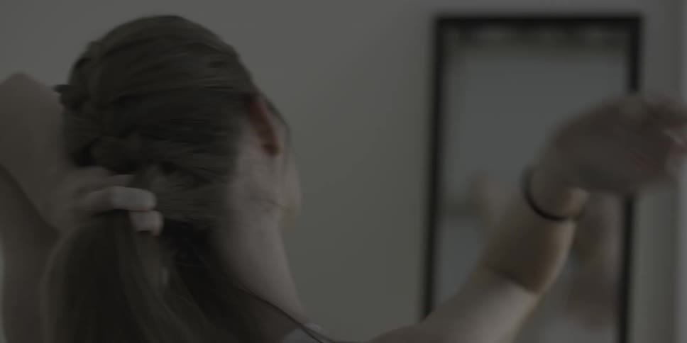 A woman braids her hair in front of a mirror
