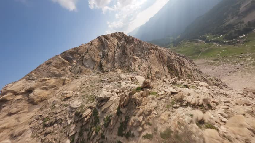 An exhilarating FPV drone flight rapidly ascends a steep, rocky mountain ridge towards the summit under a bright blue sky