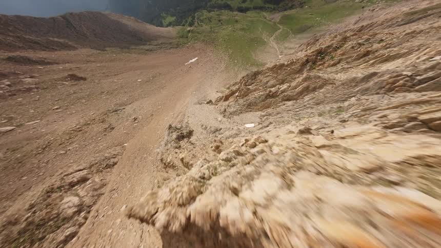 An FPV drone captures a breathtaking flight along a sharp, rocky mountain ridge before dramatically diving down its steep, sunlit slope