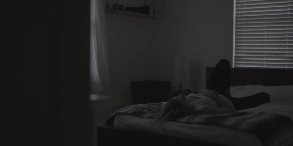 A woman lays in the bed as her curtain blows
