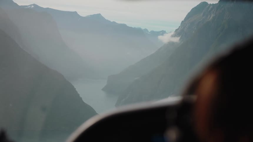 Cockpit view of a flight over a majestic, misty fjord nestled between towering mountains