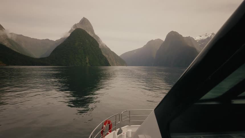 A first-person view from a boat cruising through the dramatic, misty mountains of a fjord in New Zealand