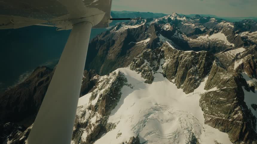A breathtaking aerial view from a small airplane flying over a vast and rugged snow-capped mountain range