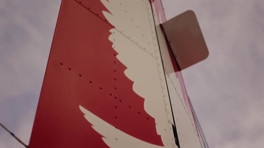 A slow upward pan reveals the red tail of a commercial airplane with a white wing logo against the sky