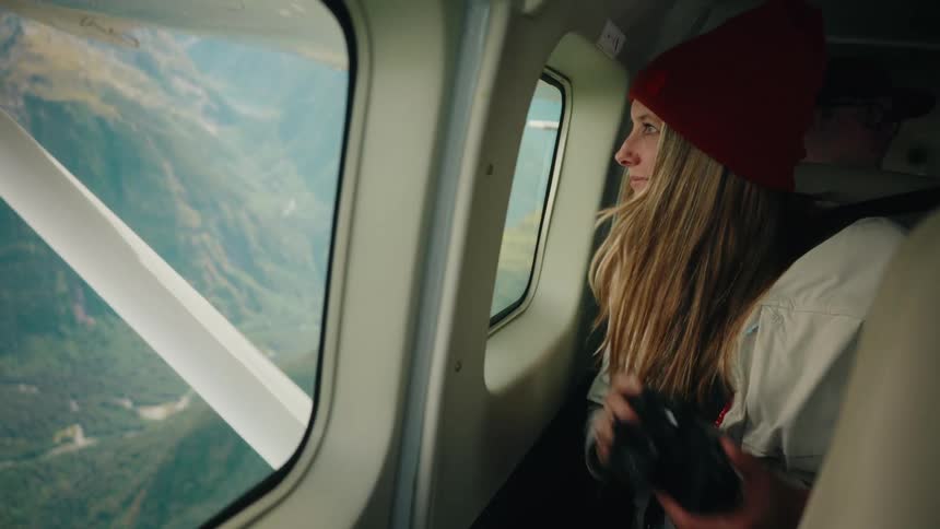 A woman with a camera in a small plane takes pictures and enjoys the stunning aerial views of the mountains below
