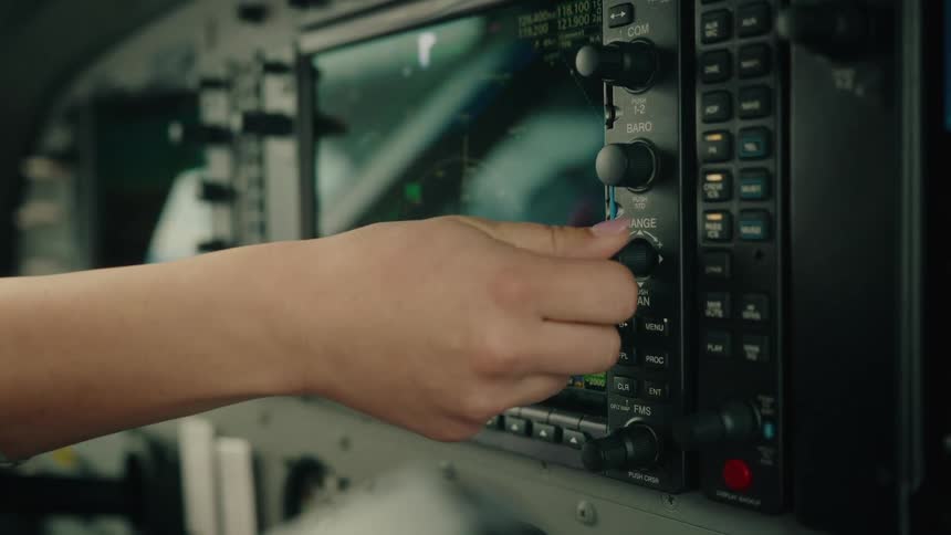A pilot's hand adjusts the knobs and buttons on the avionics control panel in a modern aircraft cockpit