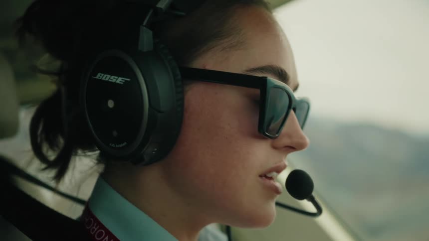 Close-up profile of a female pilot in sunglasses communicating through her headset in the cockpit
