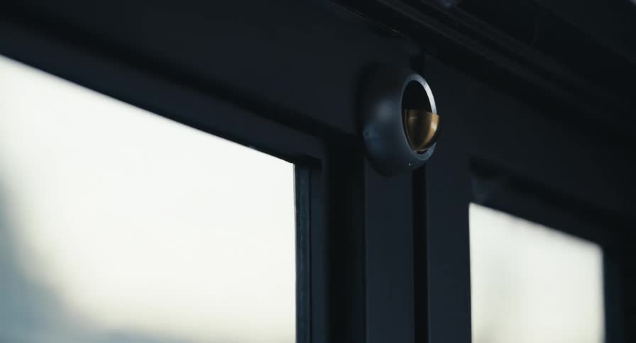 A sleek modern black door with a unique circular handle closes in slow motion against a bright window