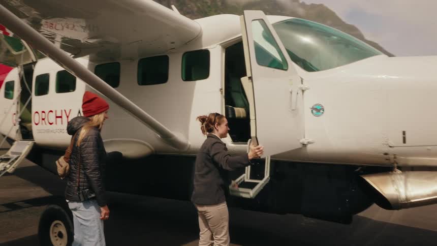 A female pilot assists a tourist boarding a small single-propeller airplane on a remote mountain airstrip