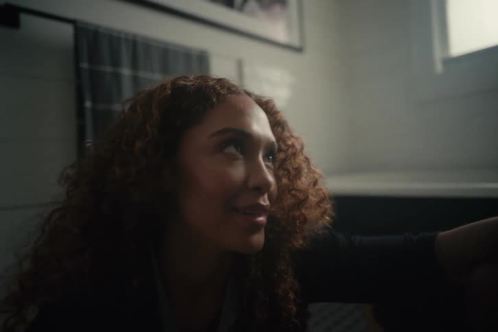 An intimate low-angle shot of a woman with curly hair talking to someone off-screen with an expression of awe