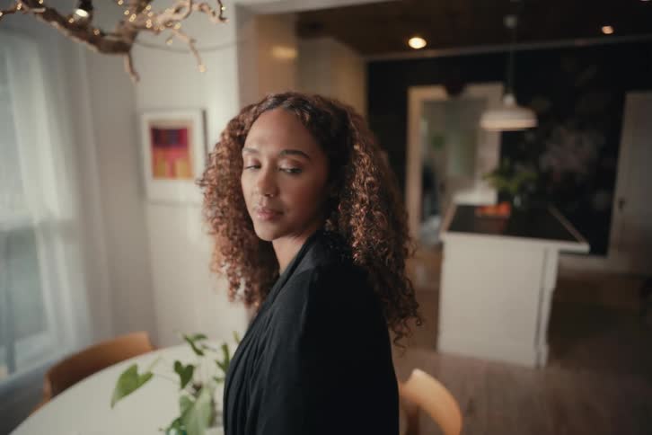 A beautiful woman with curly hair turns her head to look back and smile in slow motion in her modern home