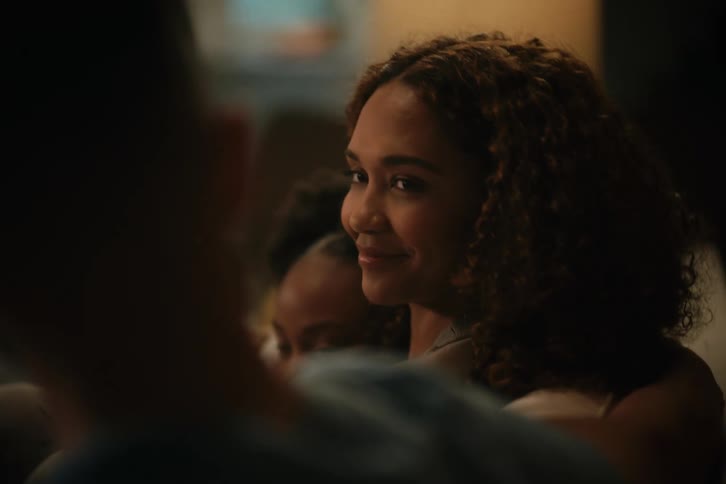 A woman with curly hair smiles lovingly at her partner during a cozy family movie night at home