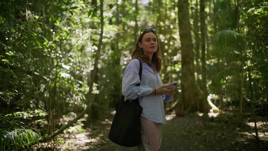 A young woman stops on a trail to admire the lush, sun-dappled forest before continuing her walk