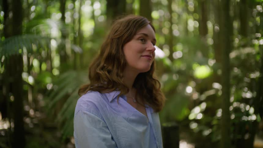 A serene woman with a gentle smile admires the beauty of a sun-dappled tropical forest