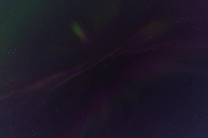 A tranquil time-lapse captures the faint, colorful dance of the aurora borealis against a backdrop of twinkling stars