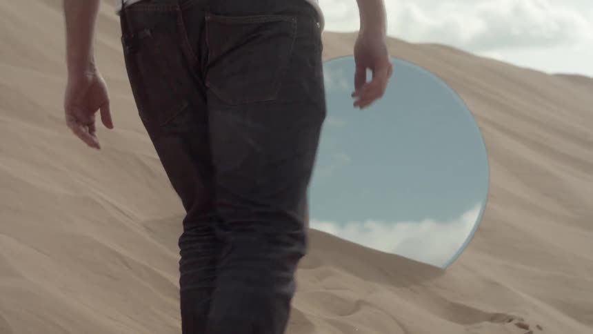 A man walks in the sand towards a mirror