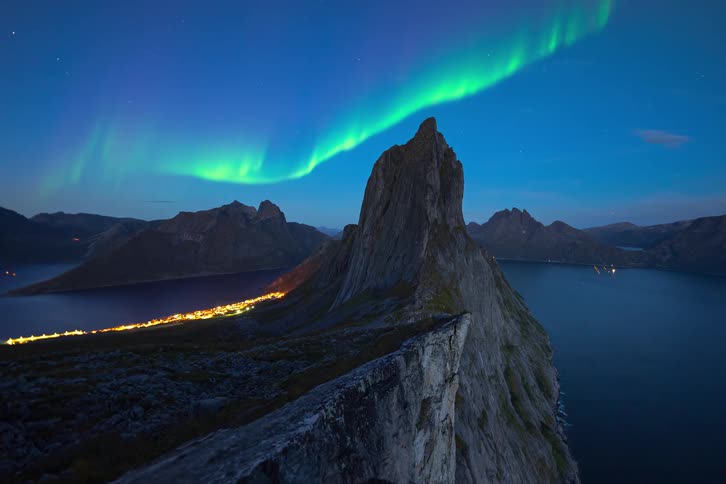 A breathtaking timelapse shows the vibrant green Northern Lights dancing over the iconic Segla mountain peak and a fjord village in Senja, Norway