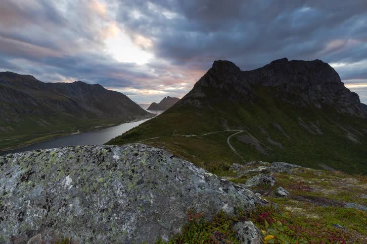 A dramatic sunset timelapse over a stunning Norwegian fjord landscape, with the sun bursting from behind a peak before setting over the ocean