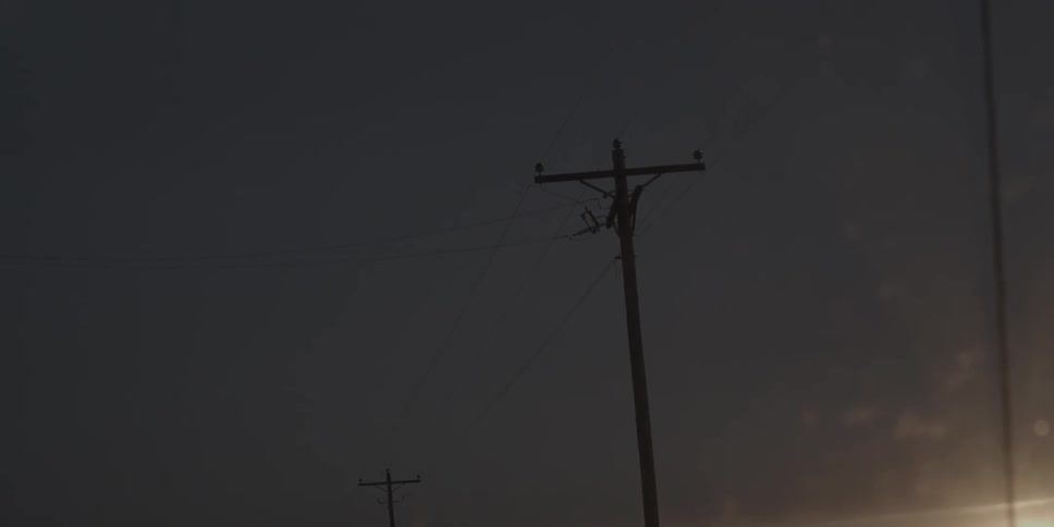 Telephone poles stand against a darkened sky along a road