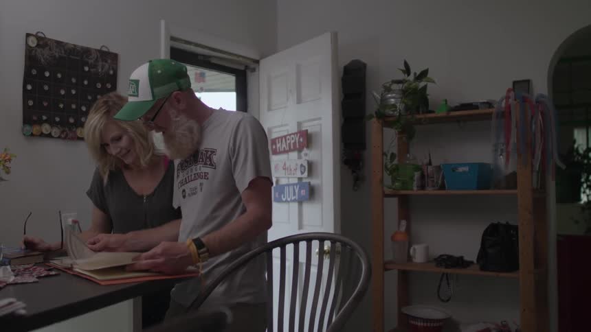 An older man and a woman are standing in a room going through a book
