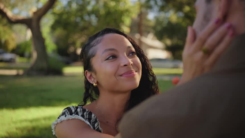 An affectionate woman holds her partner's face and smiles warmly at him in a sunlit park