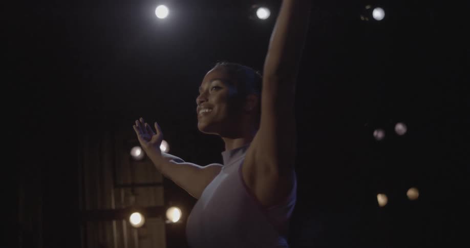Woman smiling and posing with arms in the air on dark theater stage