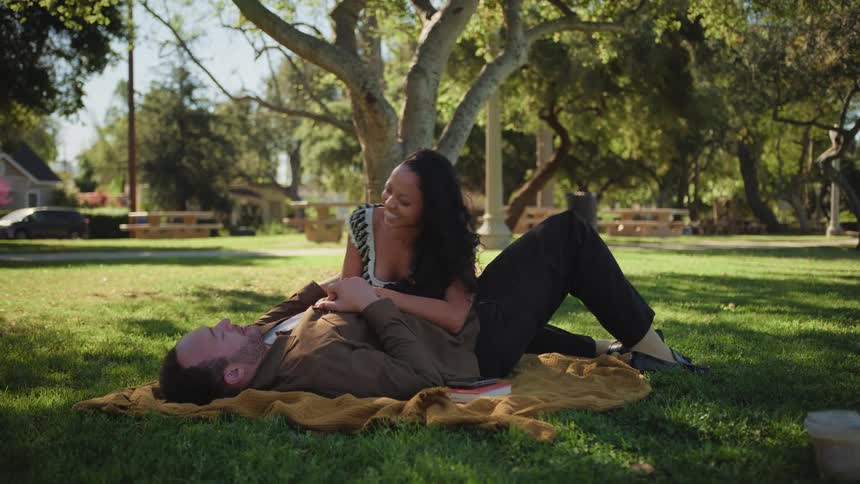 An affectionate couple enjoys a peaceful afternoon relaxing on a blanket under a tree in a sunlit park