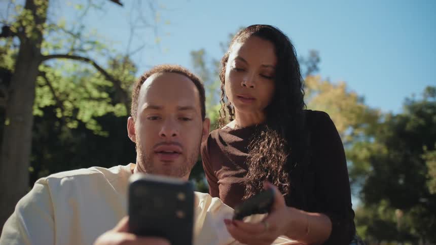 A young couple on a date in the park uses a smartphone to take a selfie or make a video call on a sunny day