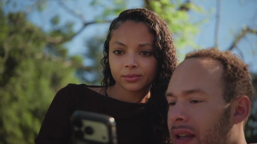 A close-up of a young couple looking at a smartphone together while enjoying a sunny day in the park