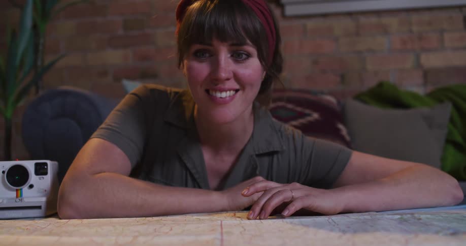 A young woman full of wanderlust excitedly plans her next adventure by tracing a route on a large map in her cozy living room