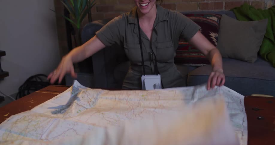 A young female explorer excitedly unfurls a large map across a table, revealing her next big adventure in dramatic slow motion
