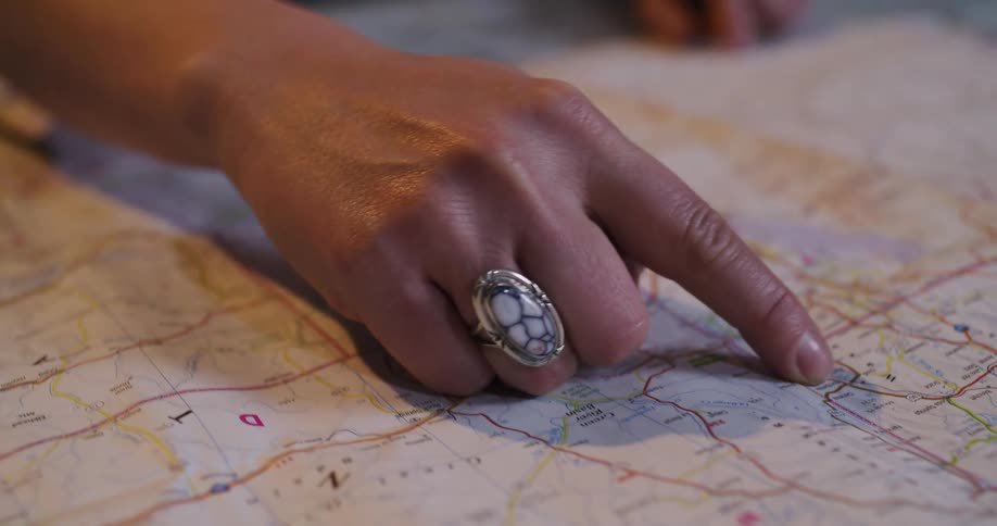 A close-up of a woman's hand with a silver ring tracing a route on a physical road map while planning a trip