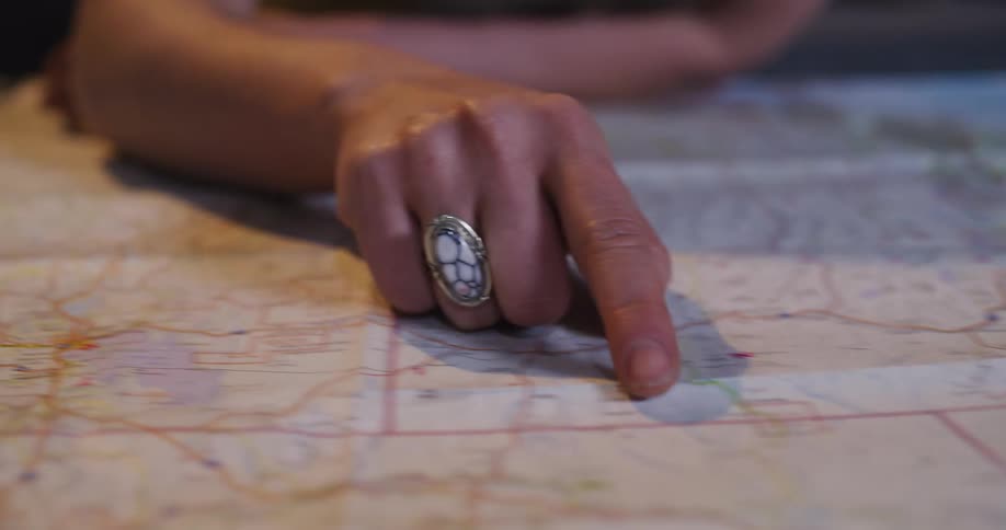 Close-up of a person's hand with a unique ring tracing a route along a road on a paper map