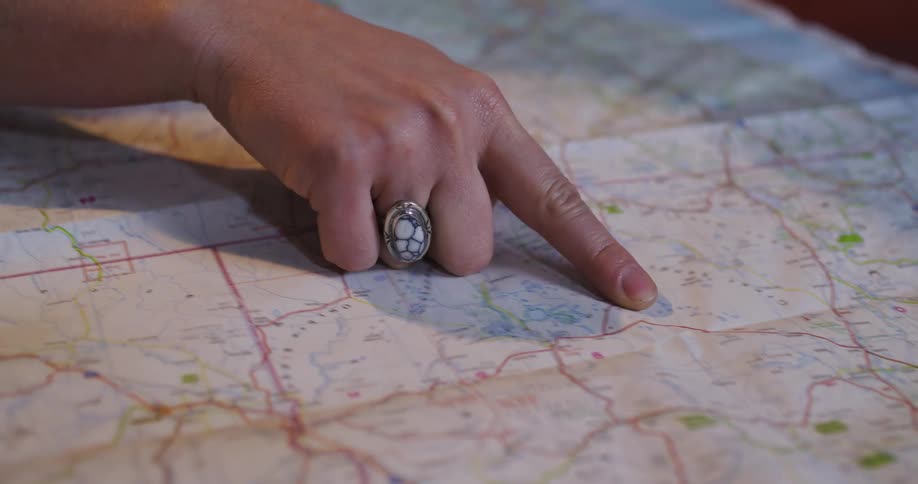 An adventurous woman carefully studies a paper road map, pointing out her destination and planning a trip