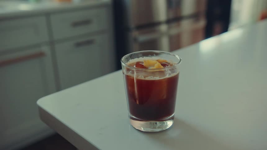 A refreshing glass of iced coffee with a citrus twist rests on a bright white kitchen counter